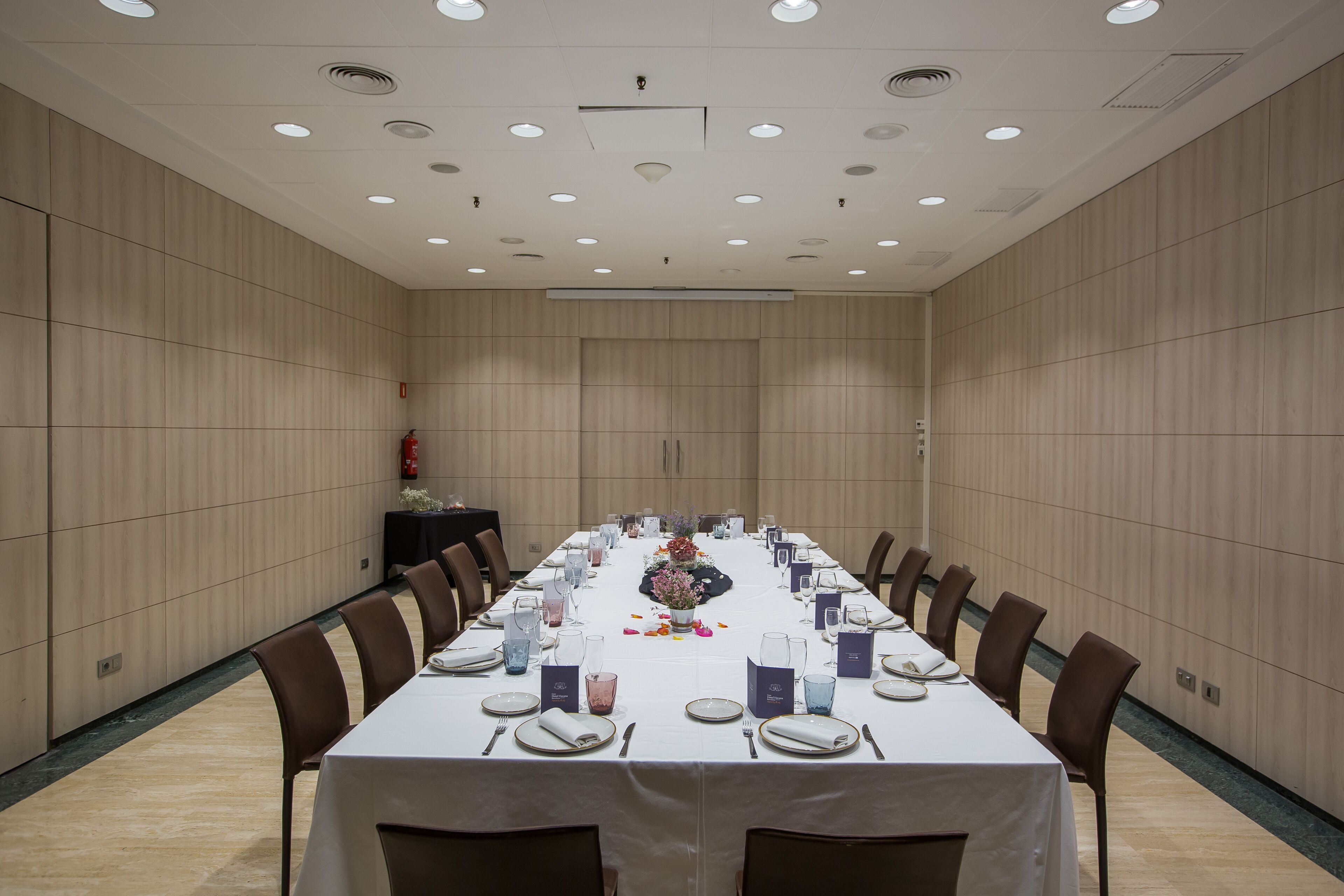 A conference room with a long table set for a meeting, equipped with chairs, nameplates, and a floral centerpiece.