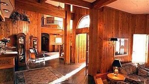 Un interior espacioso de madera con comedor, sala de estar con sofá y una escalera que sube a un nivel superior.