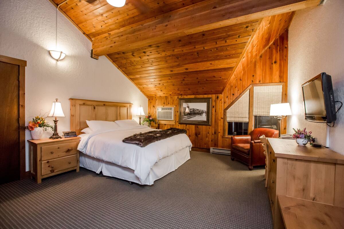 A cozy wooden room with a bed, nightstands, a desk, and a television.