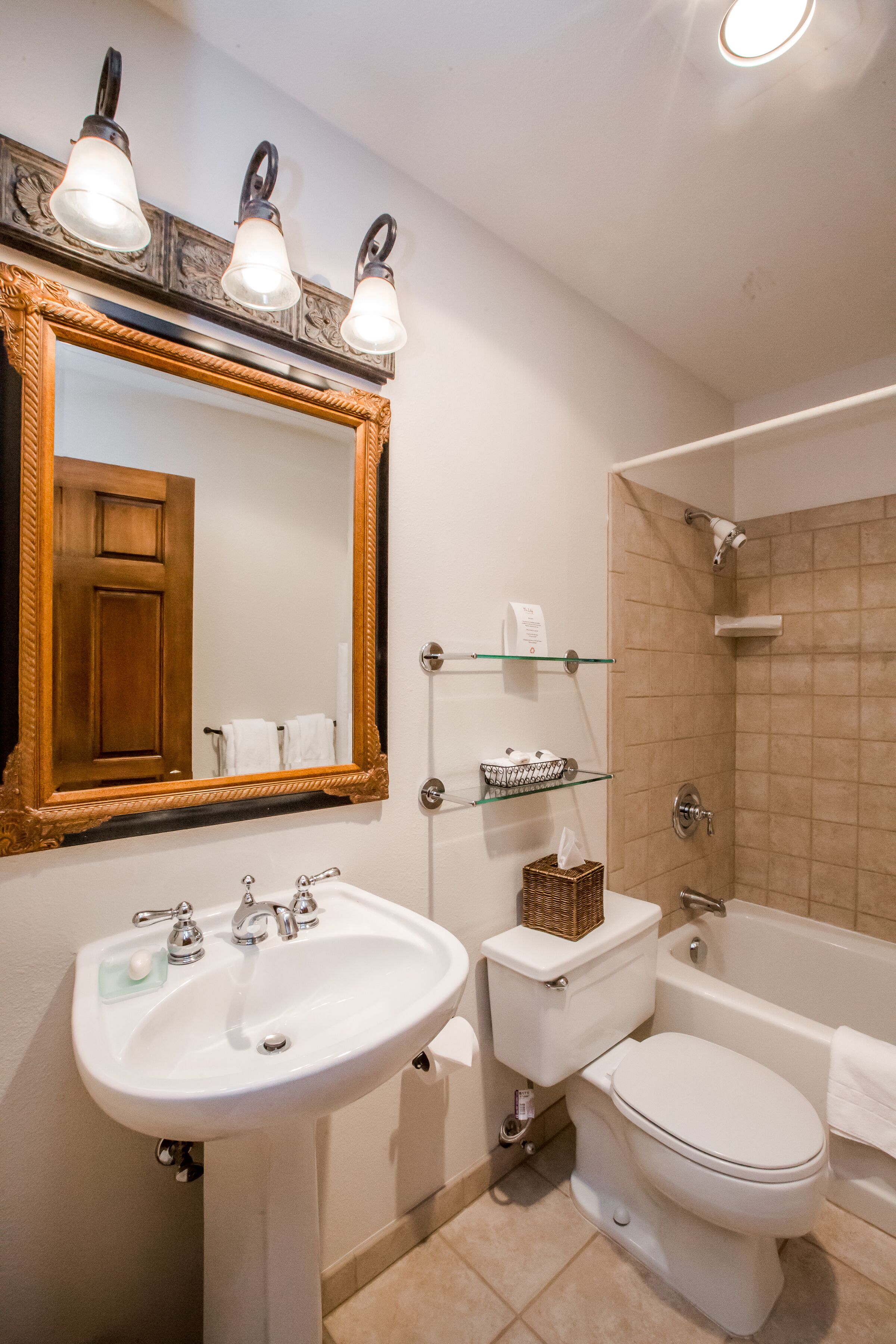 A bathroom with a sink, toilet, and bathtub. There is a mirror with a wooden frame and three light fixtures above it.