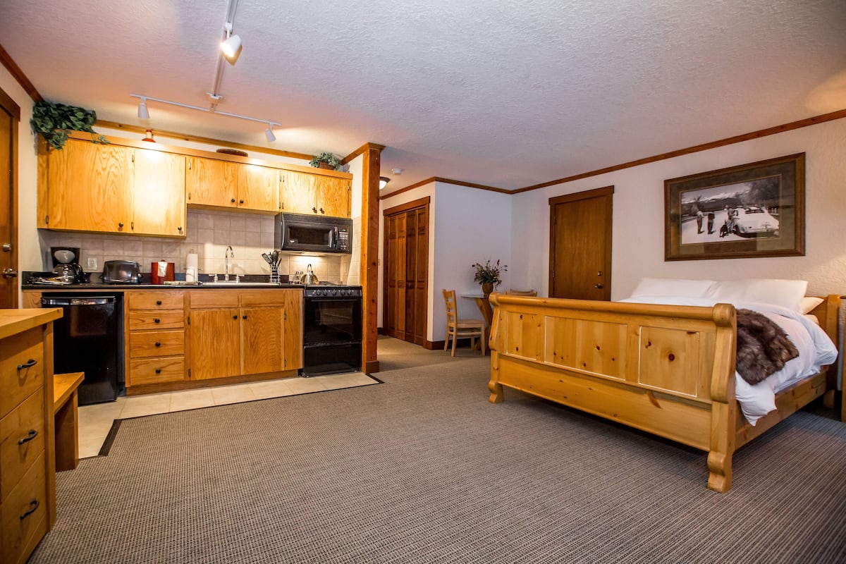 A compact room with a wooden bed, a kitchenette with a microwave, and a dining area.
