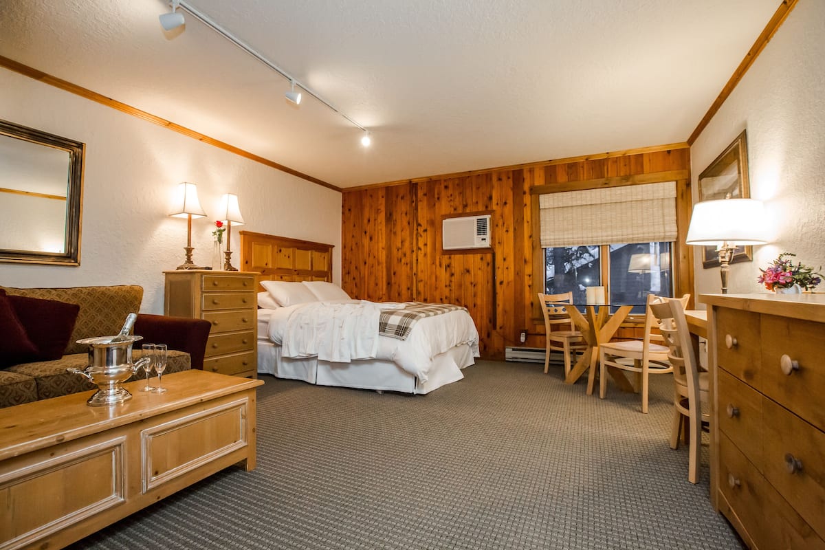 A room with a bed, a wooden dresser, a table with chairs, and a window with a view.