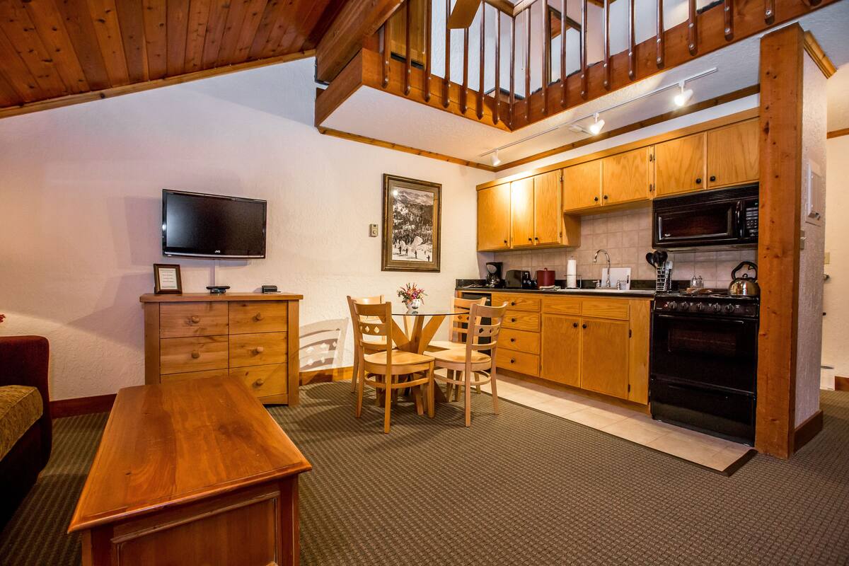 A cozy kitchen with wooden cabinets, a dining table, chairs, a TV, and a microwave.