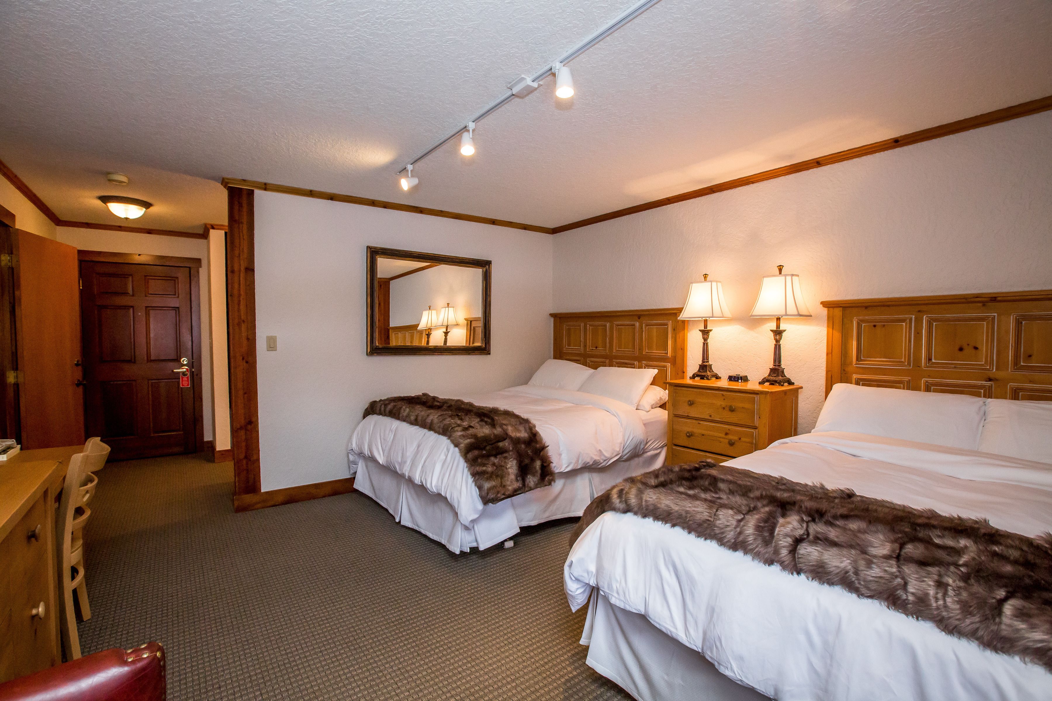 A hotel room with two beds, a wooden headboard, a mirror, and a desk with a chair.