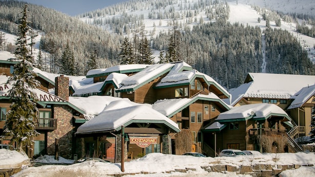 Un albergue con varias construcciones, techos cubiertos de nieve y montañas al fondo.