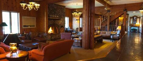 A spacious lobby with a stone fireplace, wooden beams, and a staircase.