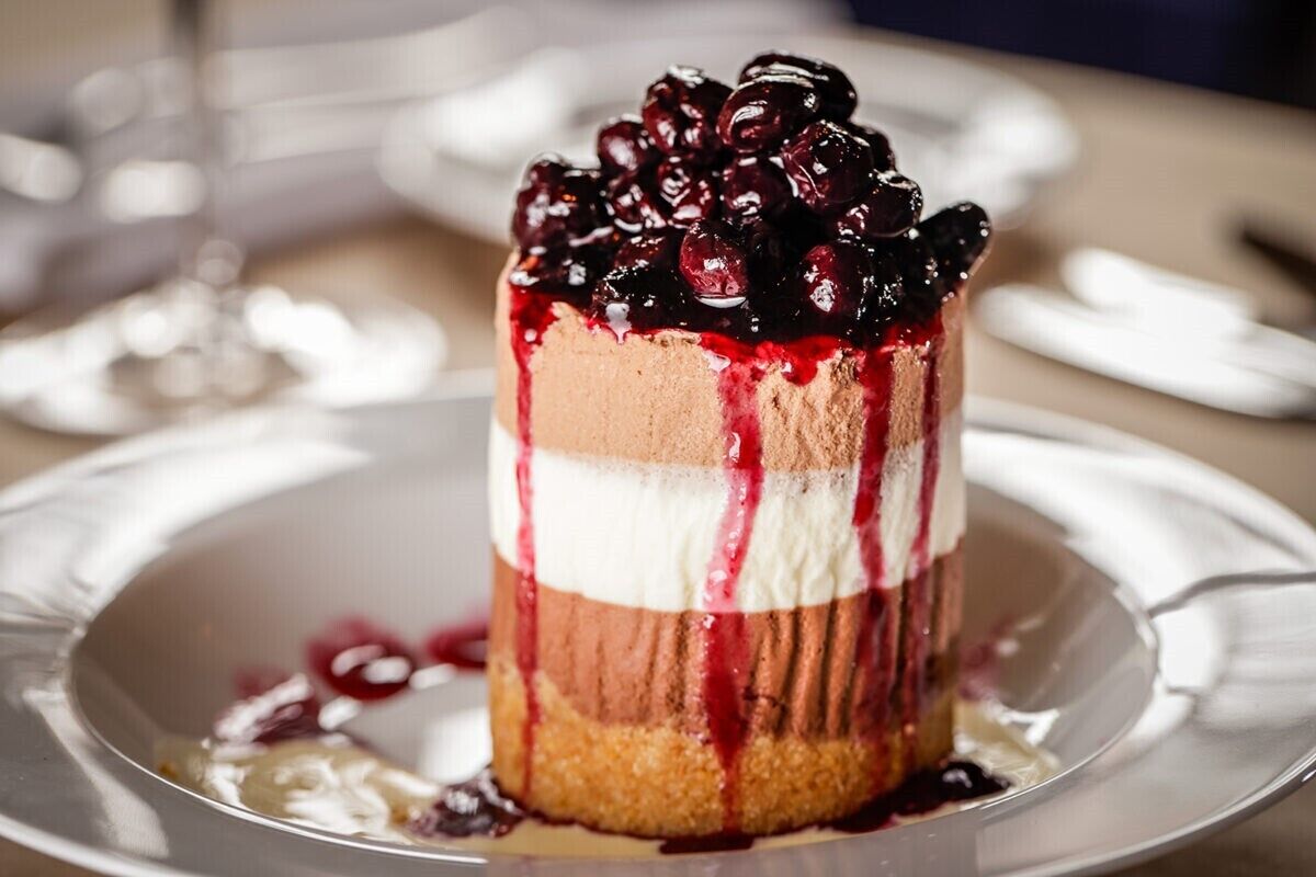 Un dessert composé de plusieurs couches, surmonté de cerises, présenté dans une assiette.