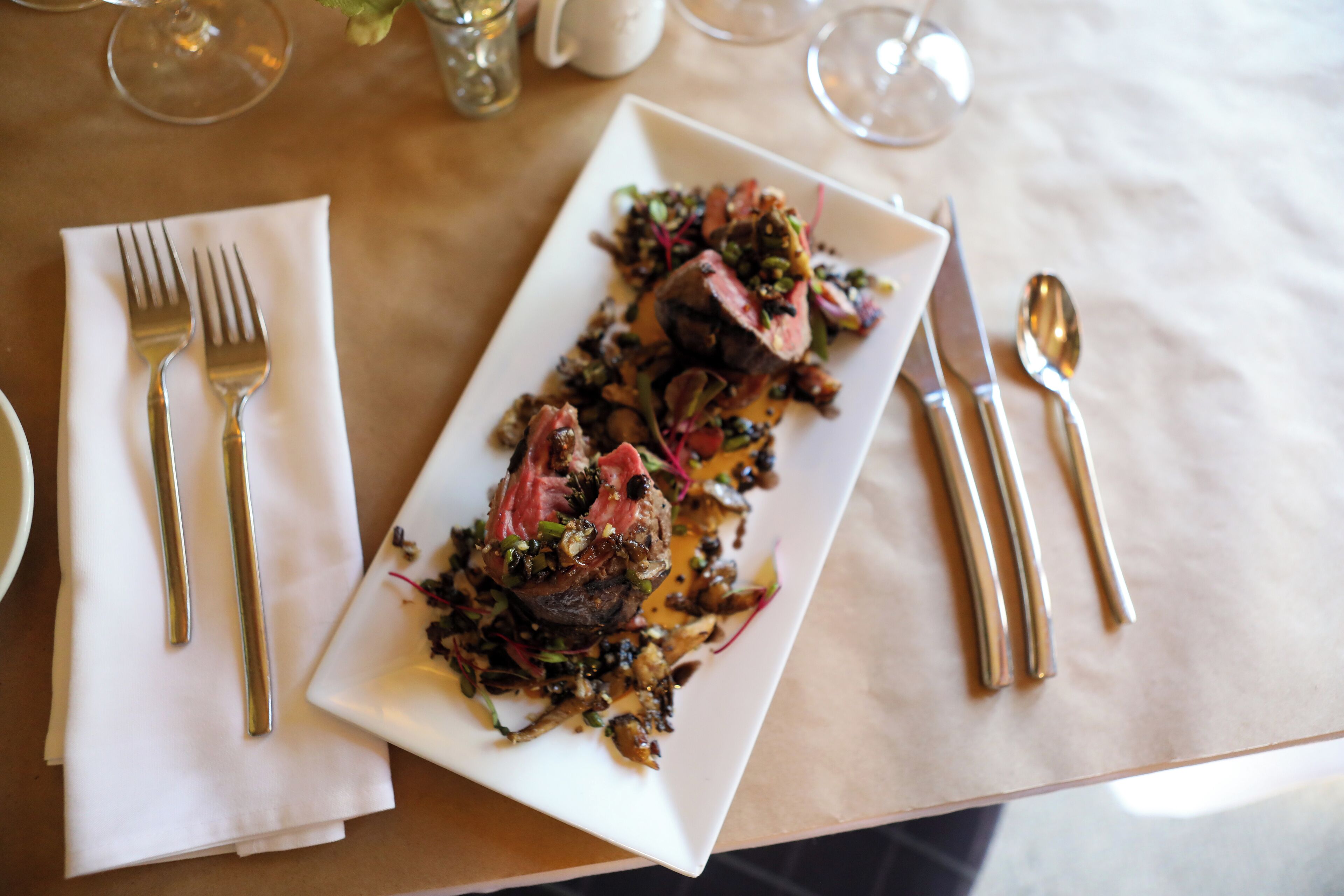 Ein rechteckiger weißer Teller mit einem Steak und Gemüse auf einem Tisch.