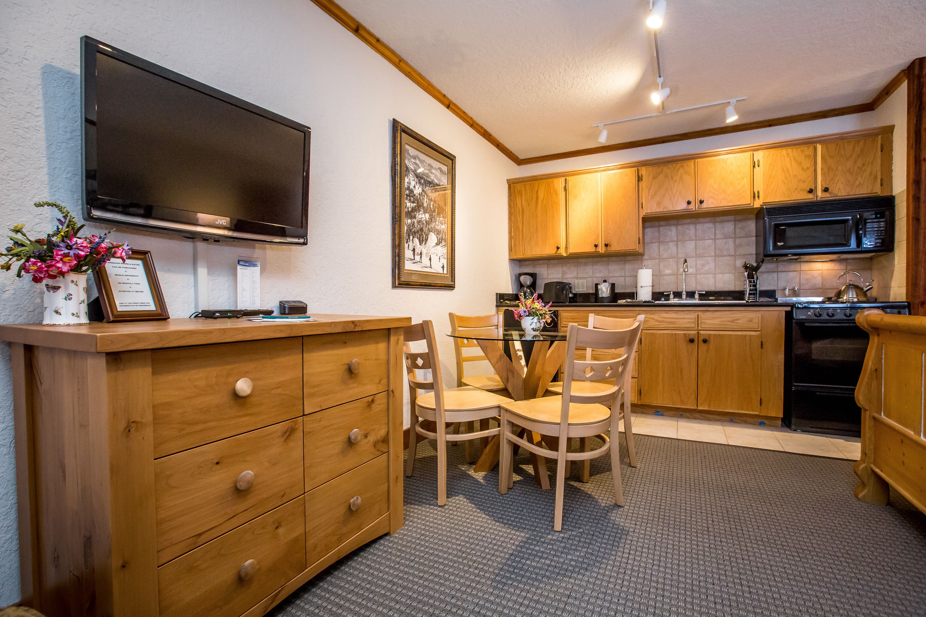 A compact kitchen with wooden cabinets, a microwave, a stove, and a dining area with chairs and a table.