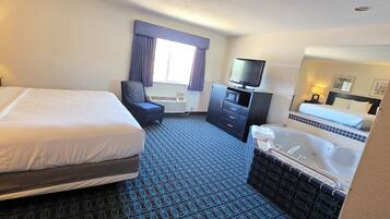 A hotel room with a large bed, a desk with a computer, a chair, a television, a microwave, a minibar, a bathroom with a bathtub, and a window with curtains.