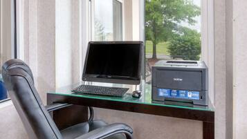 Espaço de escritório em casa com computador, impressora e cadeira perto de uma janela.