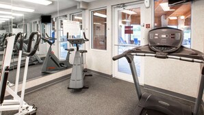 A gym with exercise equipment, a mirrored wall, and a door leading to an outdoor area. - Baymont by Wyndham Howell/Brighton (Howell)