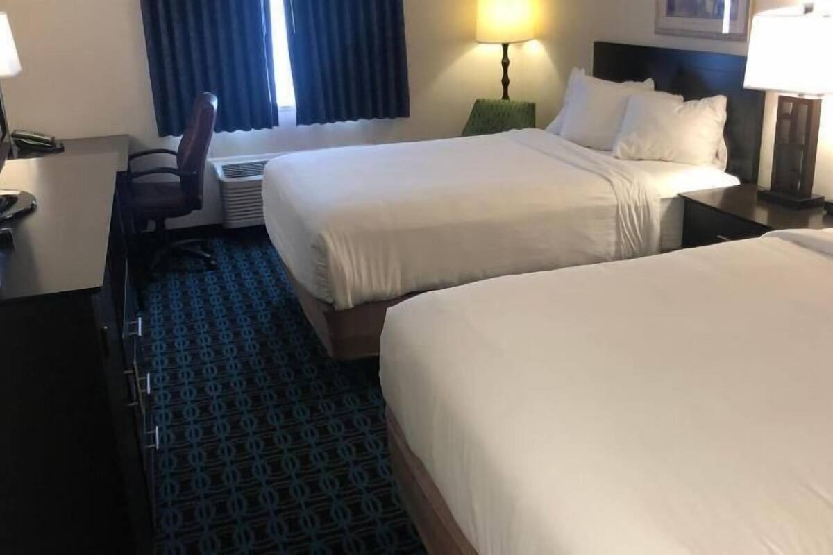 A hotel room with two beds, a desk, a chair, a lamp, and a window with curtains.
