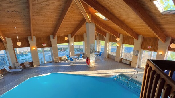 An indoor swimming pool with wooden beams and a tiled floor, surrounded by lounge chairs and tables. - Baymont by Wyndham Howell/Brighton (Howell)