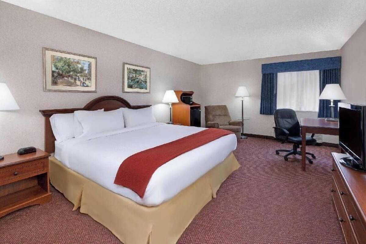 A hotel room with a large bed, a desk with a chair, a television, two lamps, and two framed pictures on the wall.
