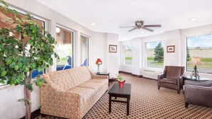 A spacious living room with a patterned carpet, a sofa, a coffee table, a chair, and a potted plant. - Baymont by Wyndham Howell/Brighton (Howell)