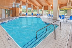 En inomhuspool med kristallklart blått vatten, omgiven av blå stolar och parasoller, och träbjälkar i taket.