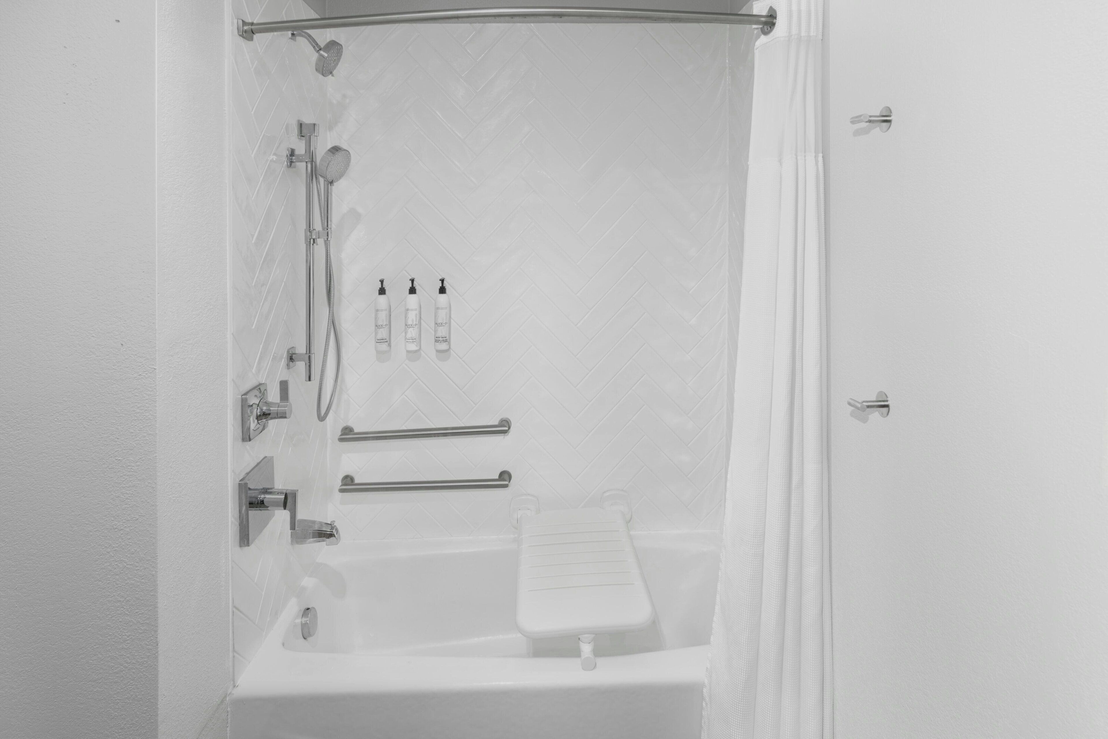 A white bathroom with a shower, a bathtub, and a toilet. There are handrails, a showerhead, and a faucet.