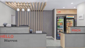 A hotel reception area with a modern design, including a reception desk labeled "Warren" and a "Marriott Bonvoy" sign. There is a Pepsi refrigerator and a "PINCH" sign indicating a vending machine. - Towneplace Suites by Marriott Warren (Warren)