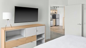 A modern hotel room with a bed, a TV mounted on the wall, a wooden console table, and a view into the kitchen area. - Towneplace Suites by Marriott Warren (Warren)