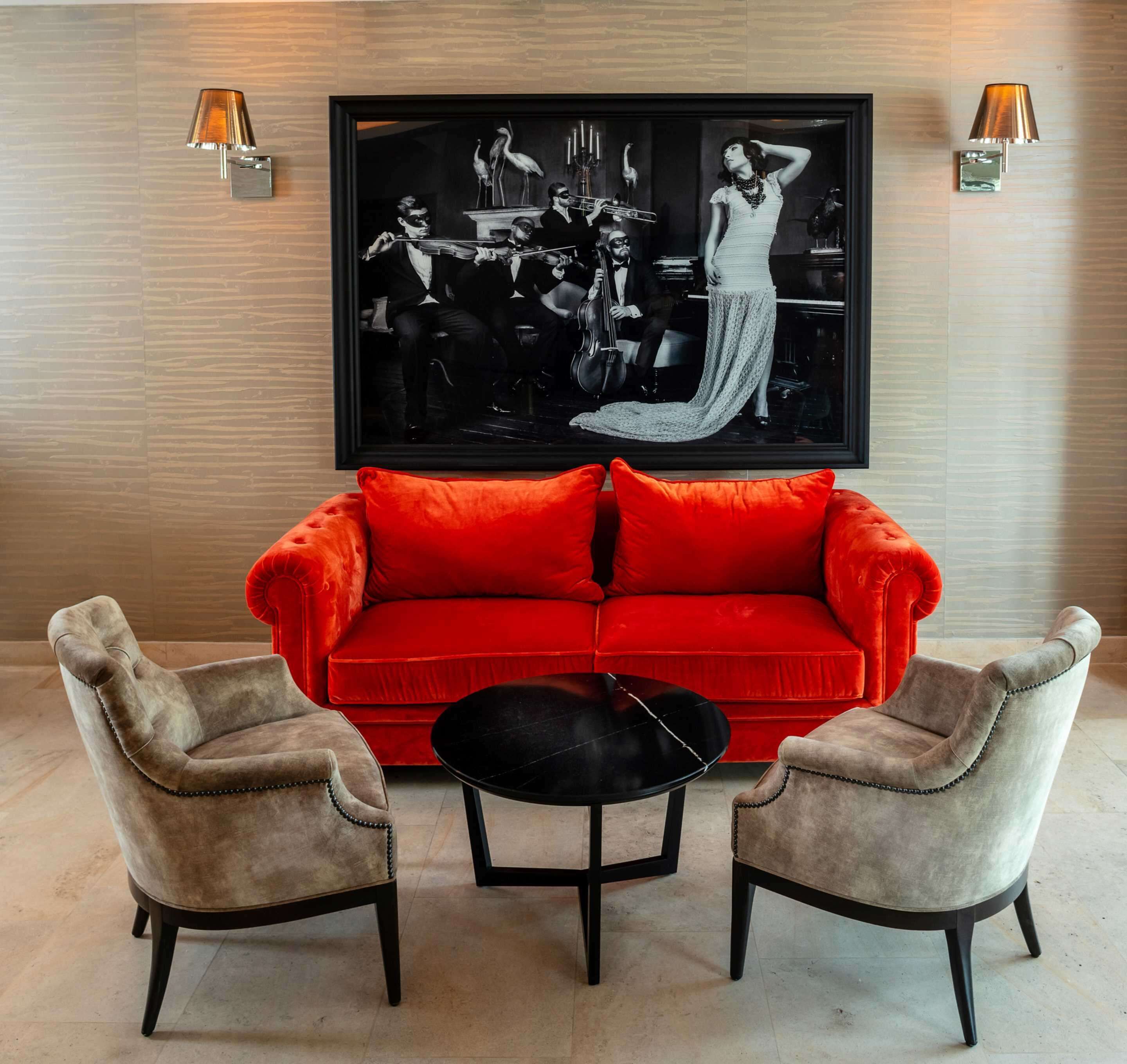 Un sofá rojo, dos sillones y una pequeña mesa negra en una habitación con un cuadro grande blanco y negro en la pared.