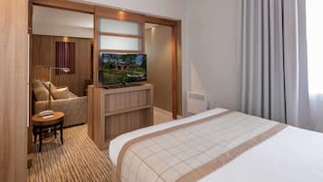 Une chambre d’hôtel avec un grand lit, un téléviseur posé sur un meuble en bois, un coin salon avec un canapé et un fauteuil, et une petite table avec un téléphone.