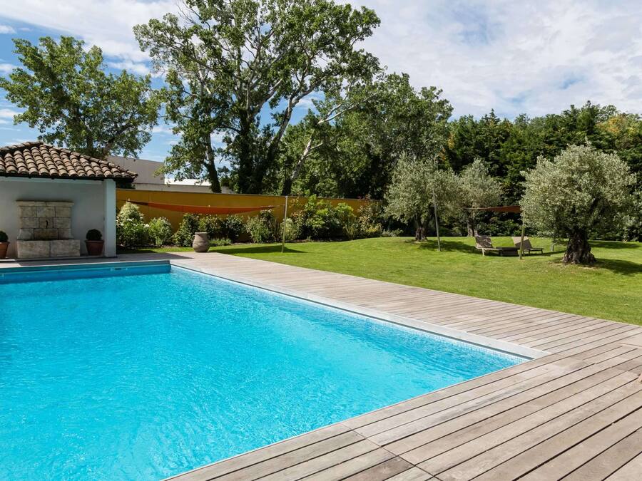 A swimming pool with a wooden deck, surrounded by a well-maintained lawn and trees.