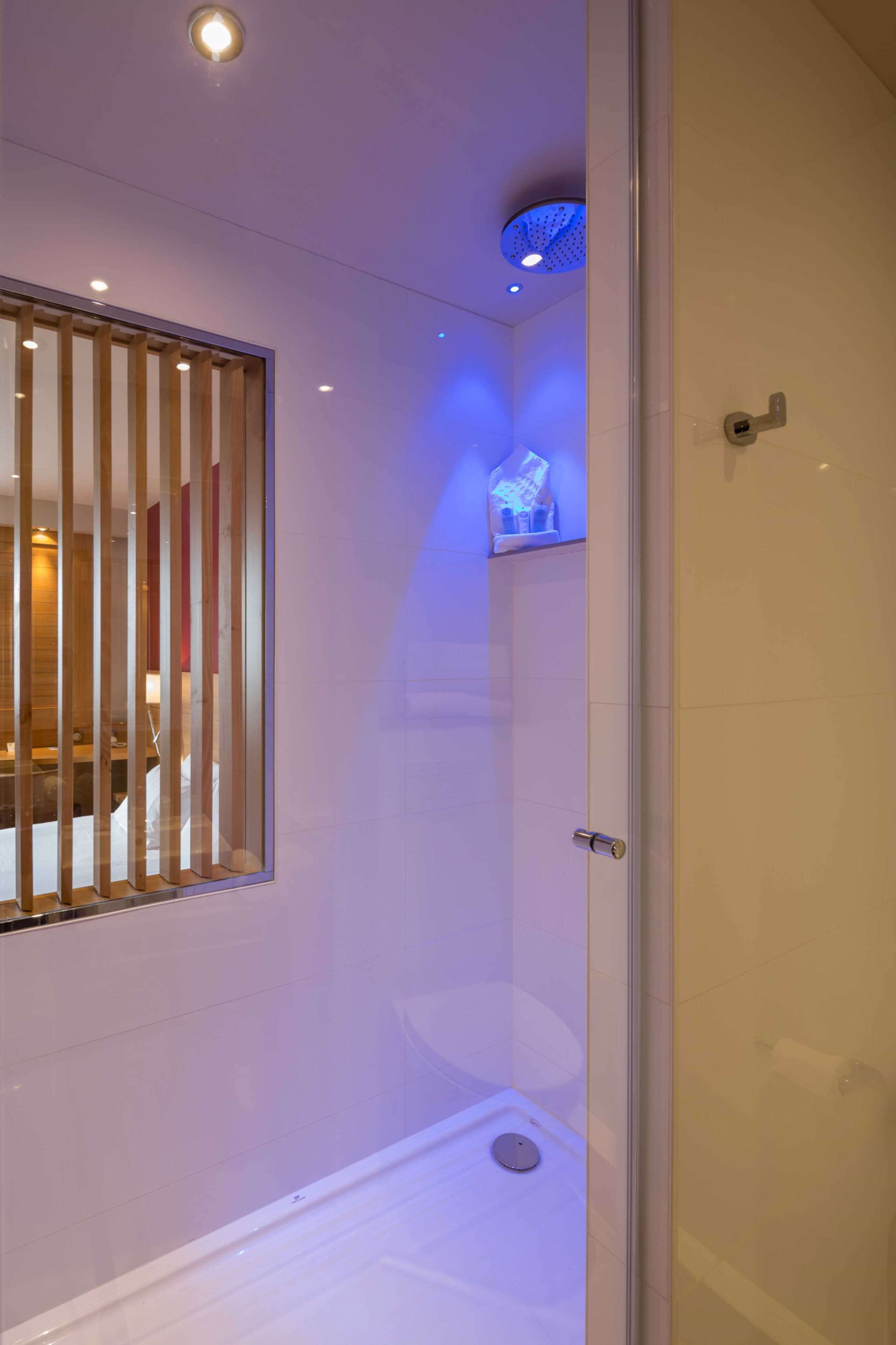 Un baño moderno con cabina de ducha de vidrio, inodoro y ventana con persianas verticales.