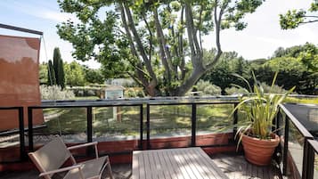 Una terraza de madera con una mesa, sillas, una planta en maceta y vistas a un jardín y árboles.