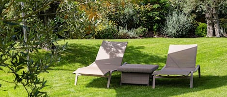 Two lounge chairs on a grassy lawn with a red umbrella overhead.