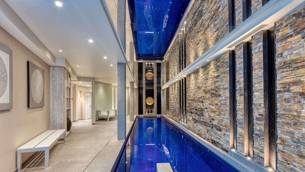 Une piscine intérieure moderne, avec un mur en pierre d’un côté et un banc de l’autre.