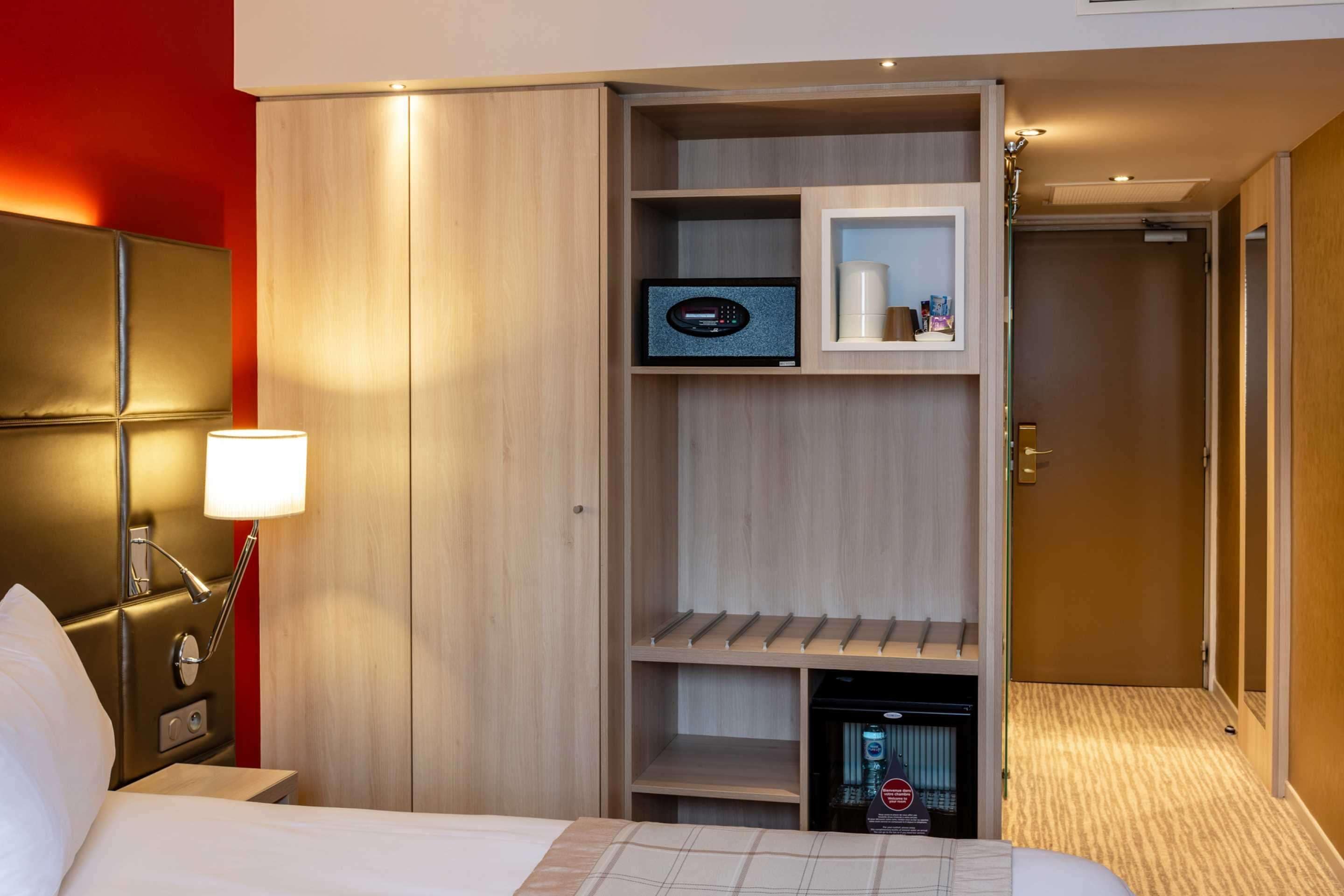 Hotelkamer met een bed, een bedlampje, een minibar, een televisie en een deur die leidt naar een andere kamer.