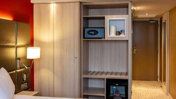 Hotelkamer met een bed, een bedlampje, een minibar, een televisie en een deur die leidt naar een andere kamer.