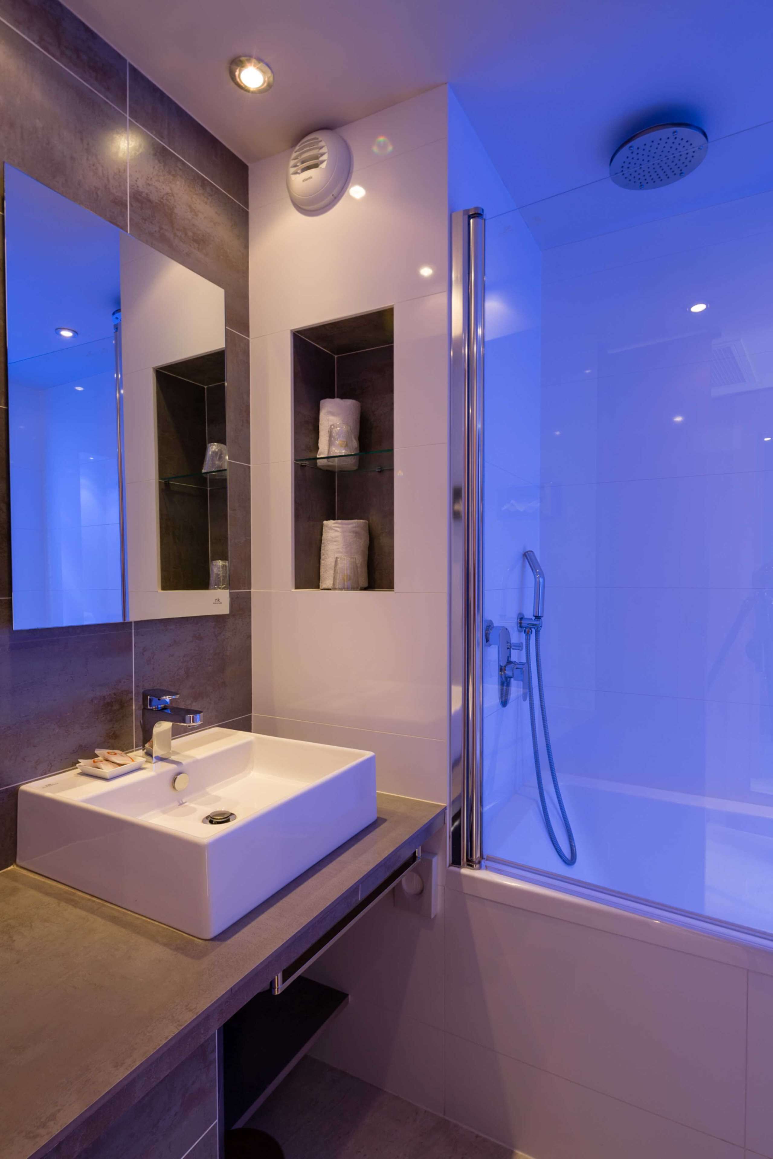 Une salle de bain moderne avec un grand miroir, un lavabo blanc et une douche à parois de verre.