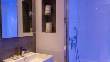 Une salle de bain moderne avec un grand miroir, un lavabo blanc et une douche à parois de verre.