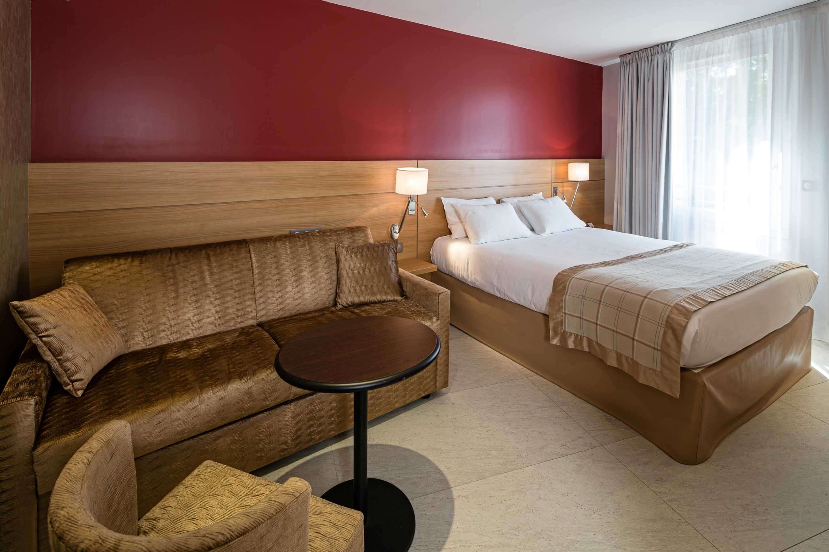 Ein Hotelzimmer mit einem Bett, einer Schlafcouch, einem kleinen runden Tisch und einem Nachttisch mit Lampen.