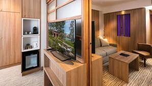 Une chambre d’hôtel moderne dotée d’une télévision à écran plat, de meubles en bois, d’un canapé et d’une petite table basse.