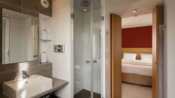 Une salle de bain moderne avec un grand miroir, un lavabo et une douche à l’italienne.