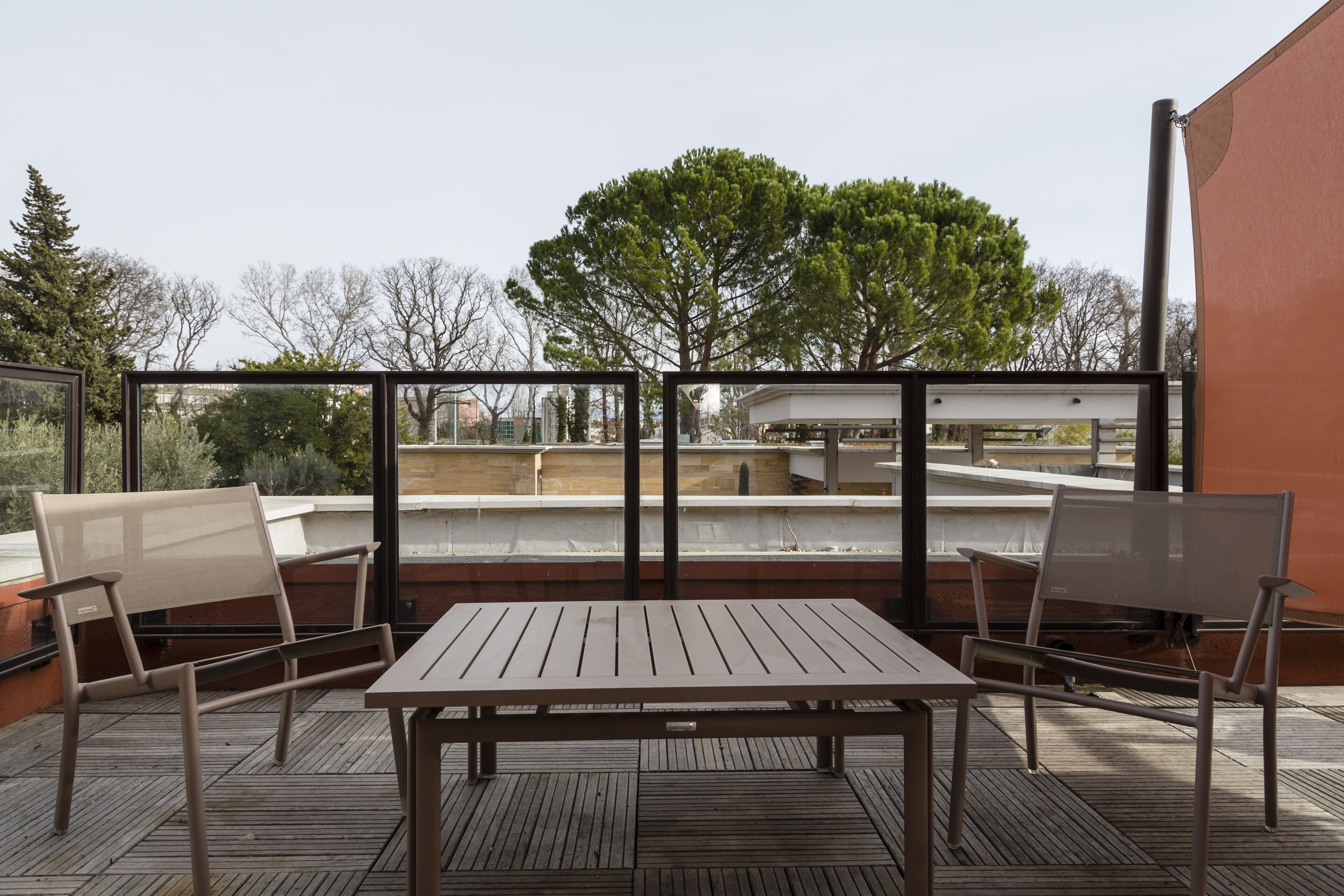 A balcony with a table and two chairs, overlooking a building and trees.