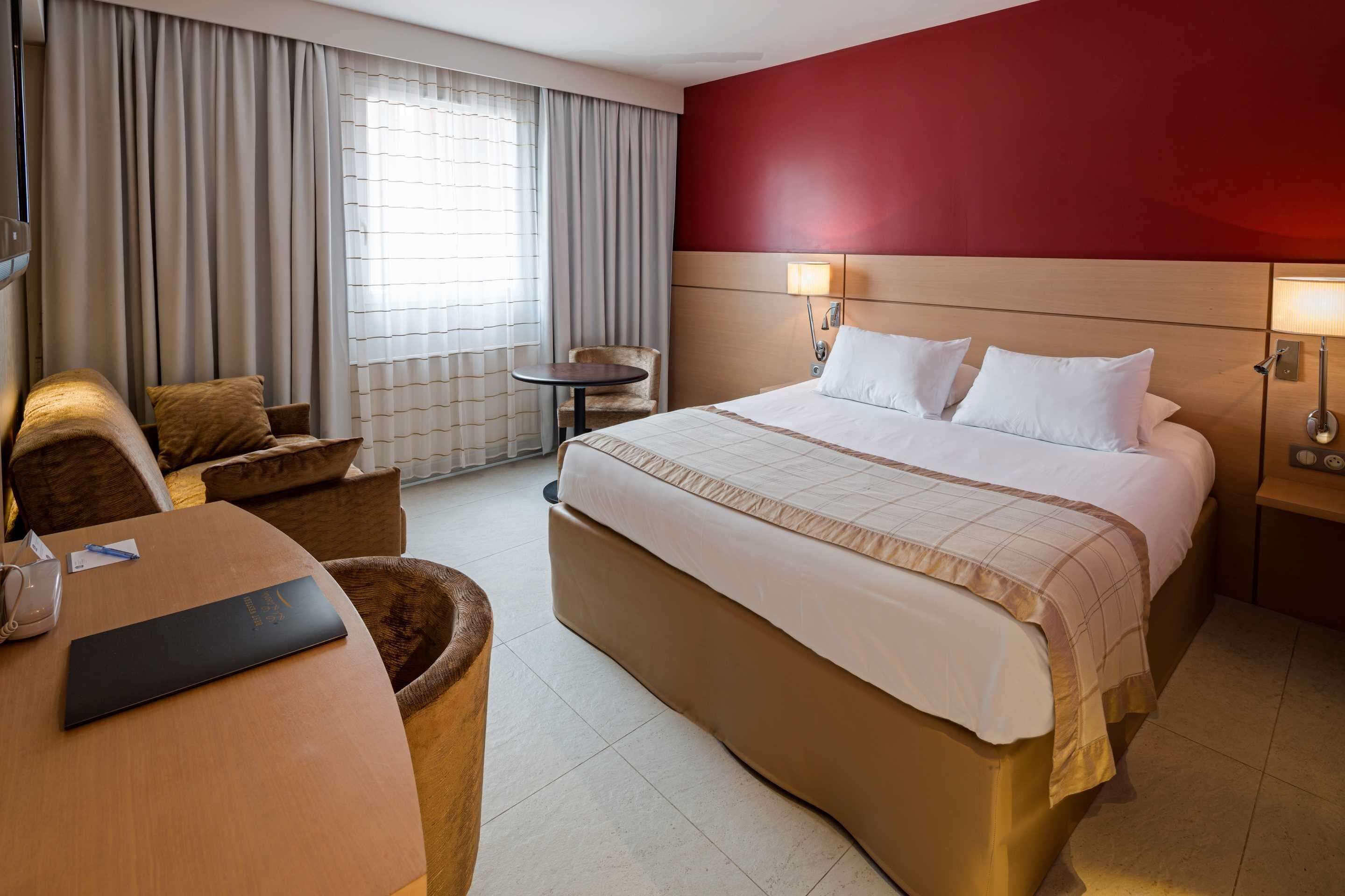 A hotel room with a large bed, a desk, a chair, and a small table.