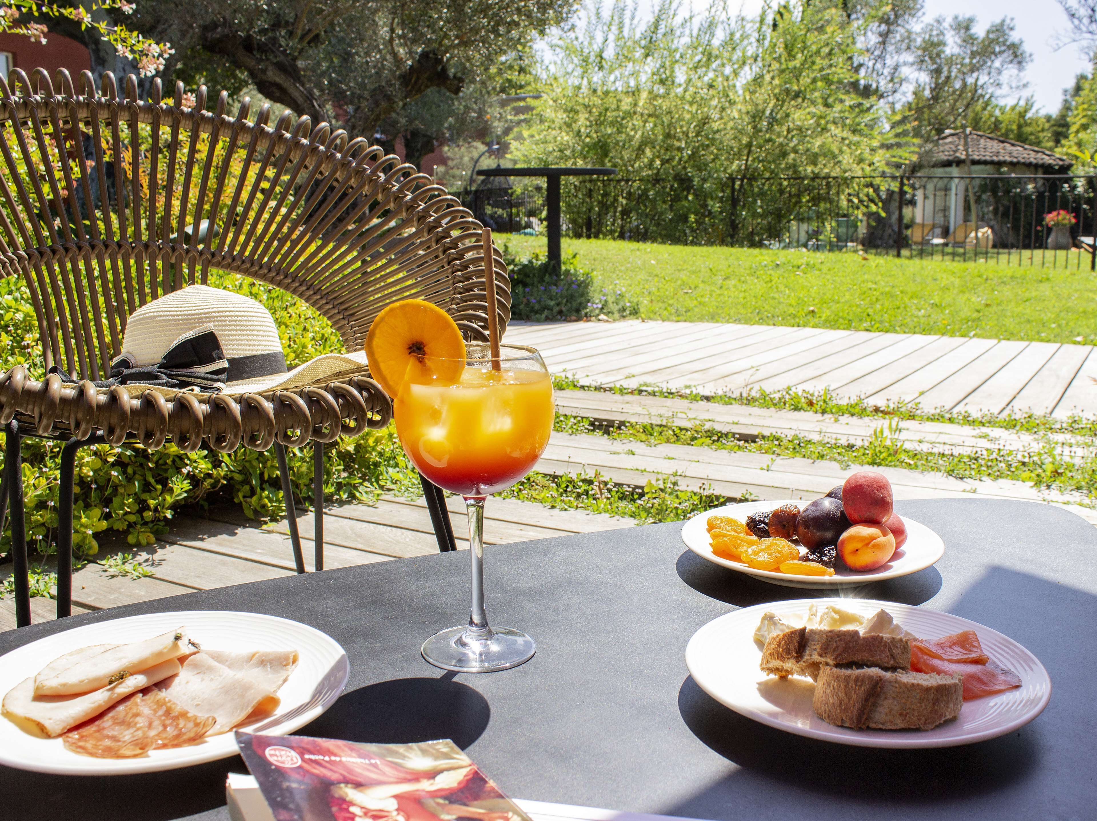 A table set outdoors with a wicker chair, a glass of drink, plates of food, and a book.