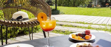 Mesa al aire libre con una silla de mimbre, un vaso de bebida, platos de comida y un libro.