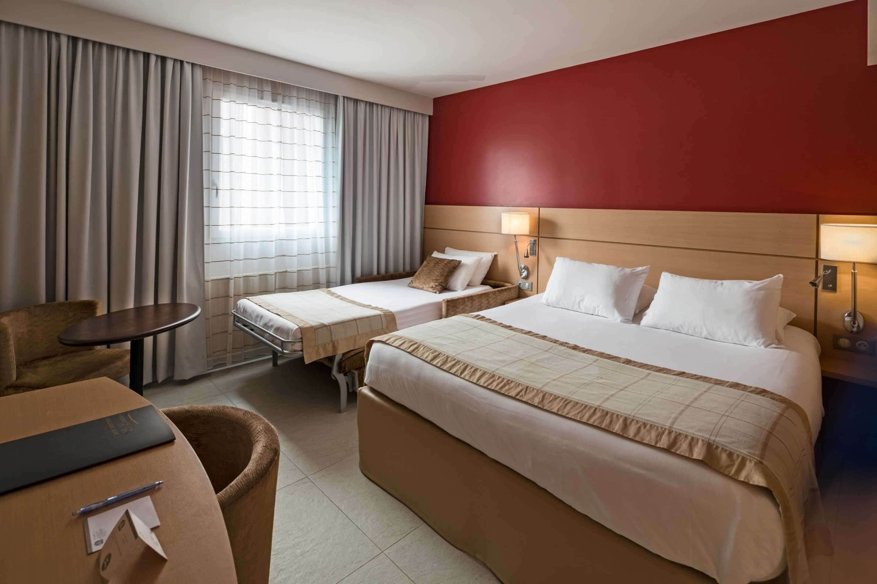 Habitación de hotel con dos camas, un escritorio, una silla y una ventana con cortinas.