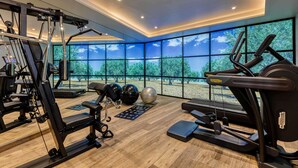 Une salle de sport moderne équipée de divers appareils d’exercice, de grandes fenêtres offrant une vue sur les arbres et d’un plancher en bois.