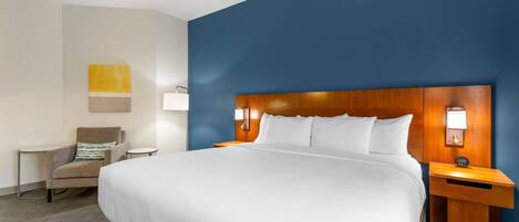 A hotel room with a large bed, a wooden headboard, bedside lamps, a chair, and a small table.