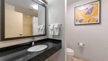 A modern bathroom with a black countertop, a white sink, a large mirror, and a toilet. There is a framed abstract art piece on the wall.
