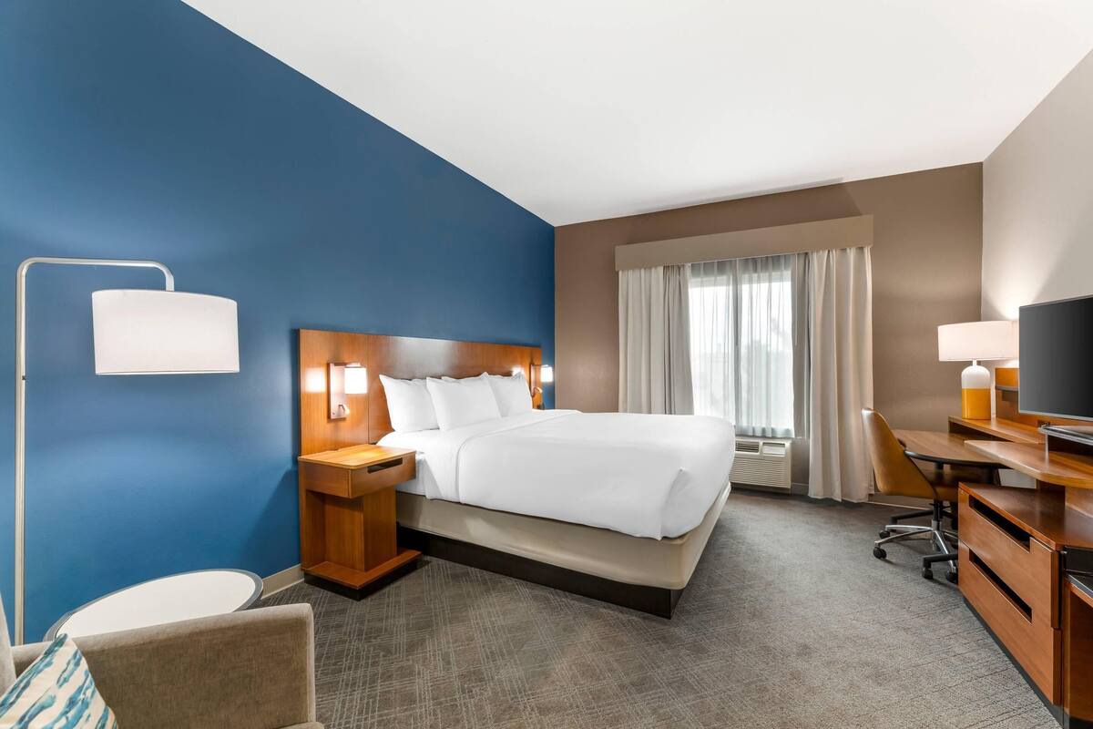 A hotel room with a large bed, a desk, a chair, a TV, and a window with curtains.