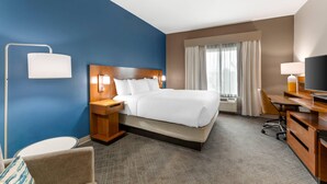 A hotel room with a large bed, a desk, a chair, a TV, and a window with curtains.
