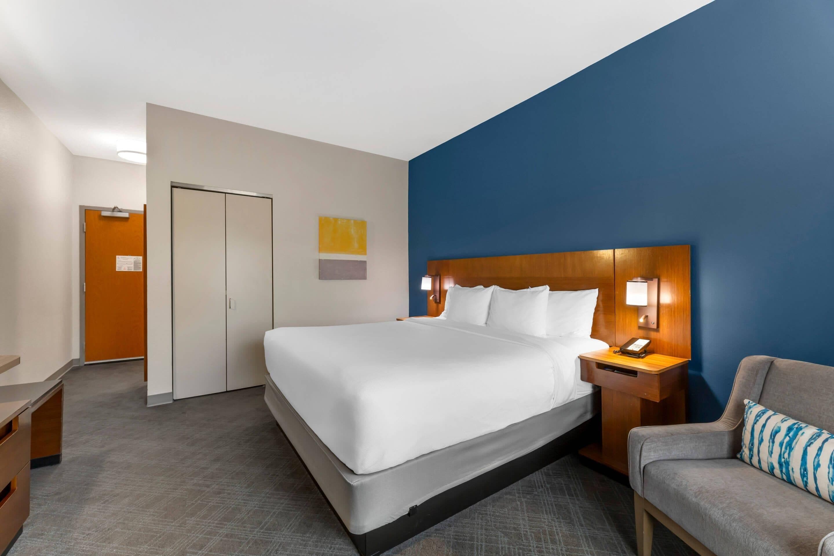A hotel room with a large bed, a desk, a chair, and a wardrobe.