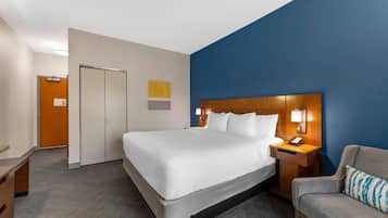 A hotel room with a large bed, a desk, a chair, and a wardrobe.